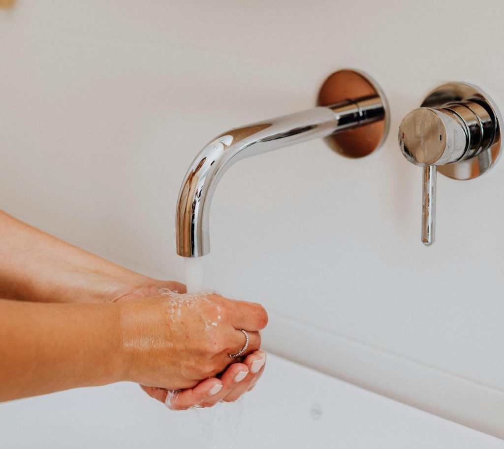 Manos lavándose bajo un grifo moderno, centrándose en la higiene y el flujo de agua.